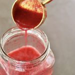 Prickly Pear Vinaigrette in a jar with more being drizzled in from a gold tablespoon.