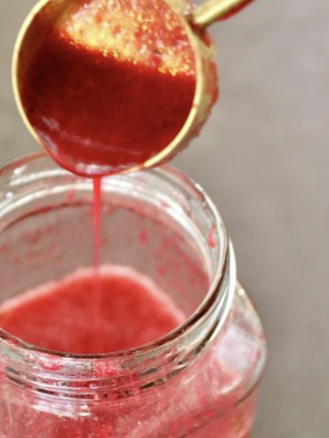 Prickly Pear Vinaigrette in a jar with more being drizzled in from a gold tablespoon.