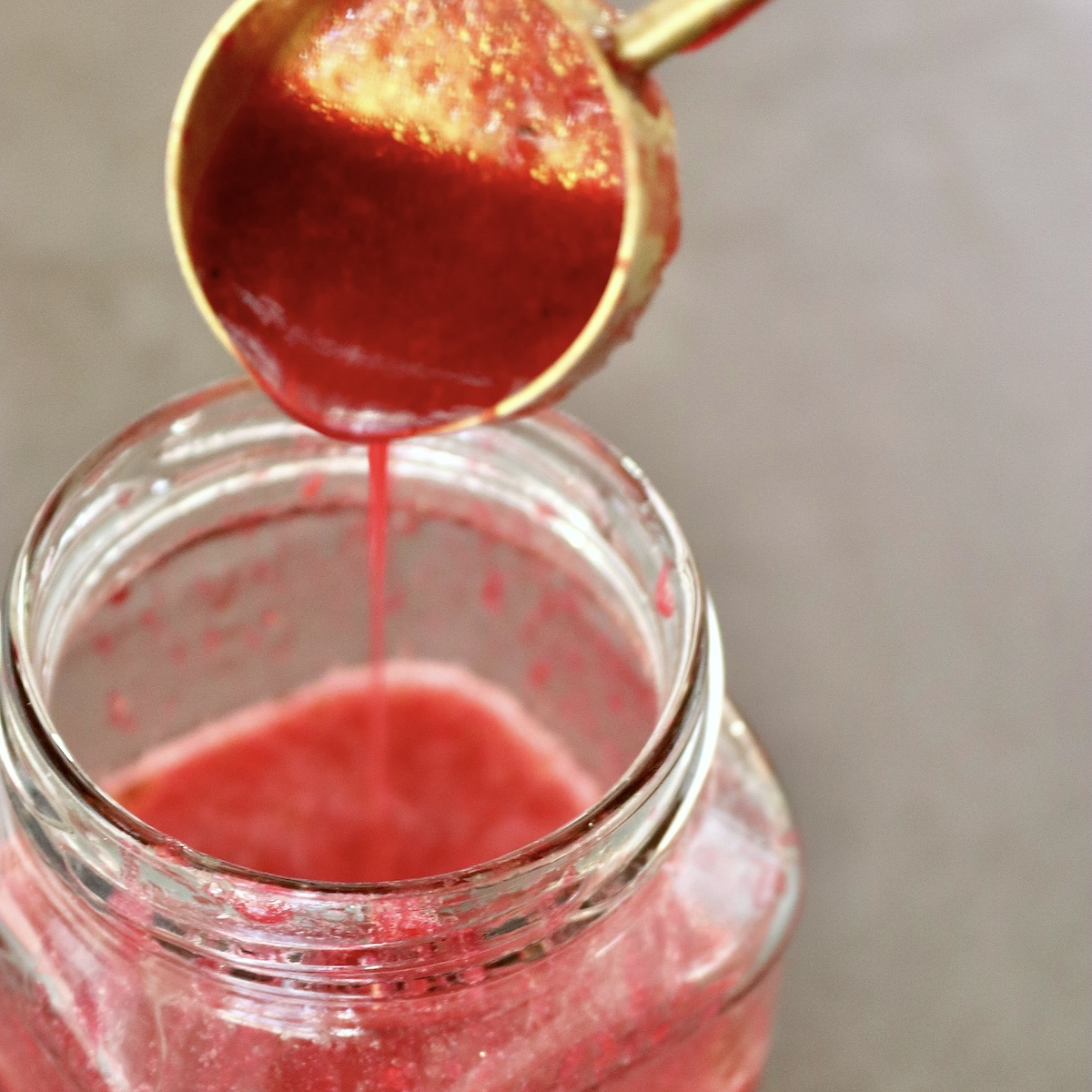 Prickly-Pear-Vinaigrette Prickly Pear Vinaigrette in a jar with more being drizzled in from a gold tablespoon.