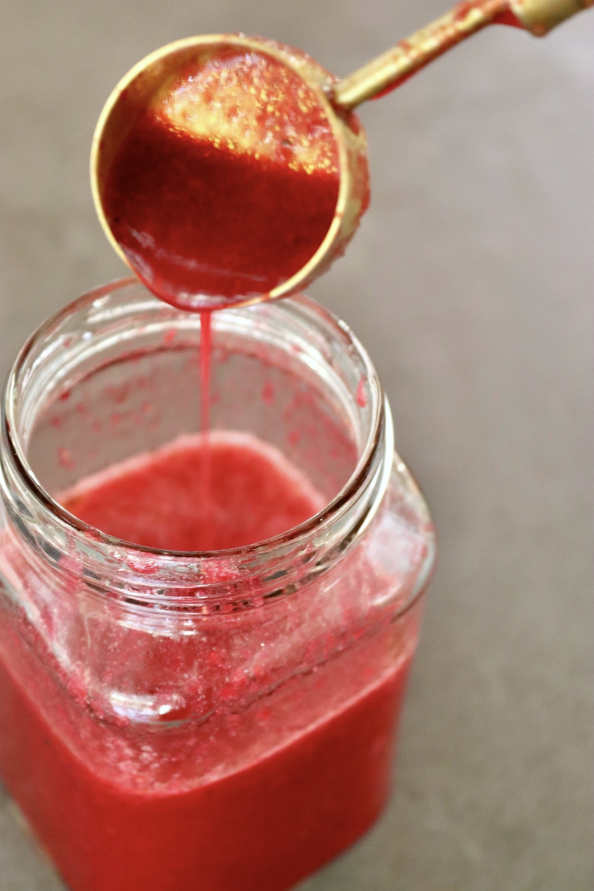 Prickly Pear Vinaigrette in a jar with more being drizzled in from a gold tablespoon.