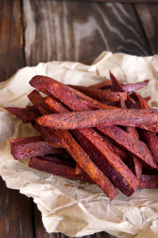 Bunch of purple French fries on crumpled parchment on wood background.