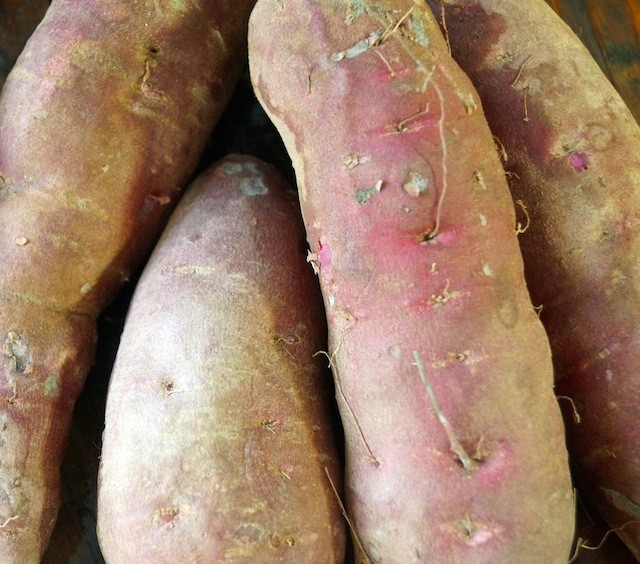 four raw slightly dirty purple sweet potatoes