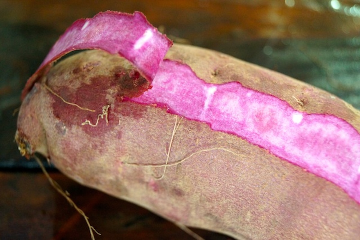 Raw, stokes purple sweet potato, with part of the skin peeling back to show bright magenta flesh.