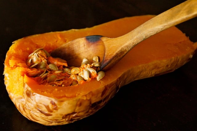 half of roasted butternut squash with wooden spoon removing seeds