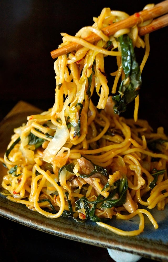 Generous serving of Chinese Longevity Noodles with Gai Lan on ceramic plate with bite in chopsticks