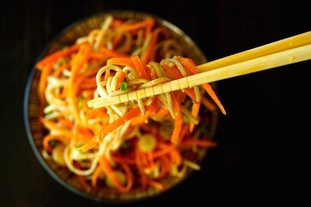 Carrot Ginger Soba Noodles in a bowl with a bite being help in chopsticks above it.