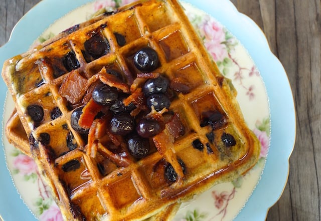Top view of a stack of Brown Butter Blueberry Bacon Waffles on antique pink and blue plate.