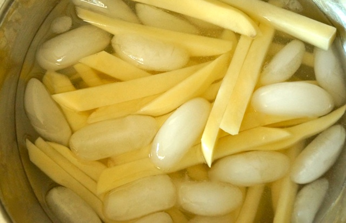 Raw potatoes cut into sticks for fries, in ice water.