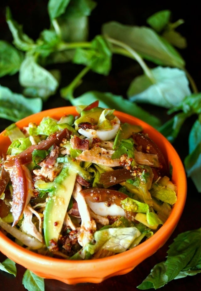 Shredded Chicken Cobb Salad in an orange bowl with fresh basil leaves.