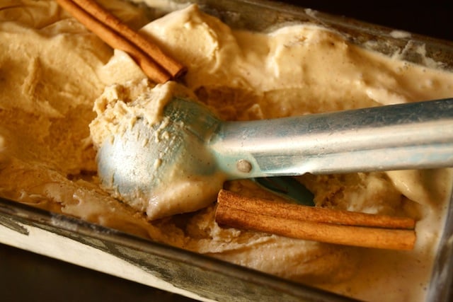 Cinnamon Ice Cream in a loaf pan with 2 cinnamon sticks nad shiny, light blue ice cream scoop.