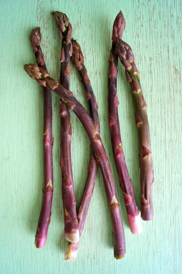 Several spears of dark purple asparagus on a minty green-colored, wooden background. 