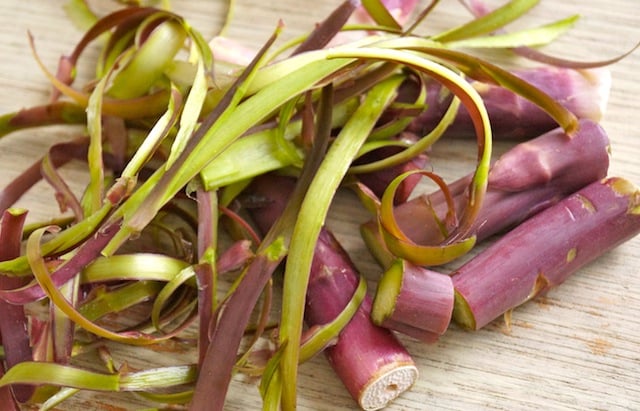 Peels and stems from purple asparagus in a pile on a cutting board.