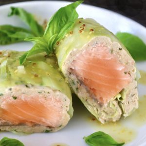 One Salmon Cabbage Roll sliced in half on a white plate with basil leaves and orange vinaigrette.