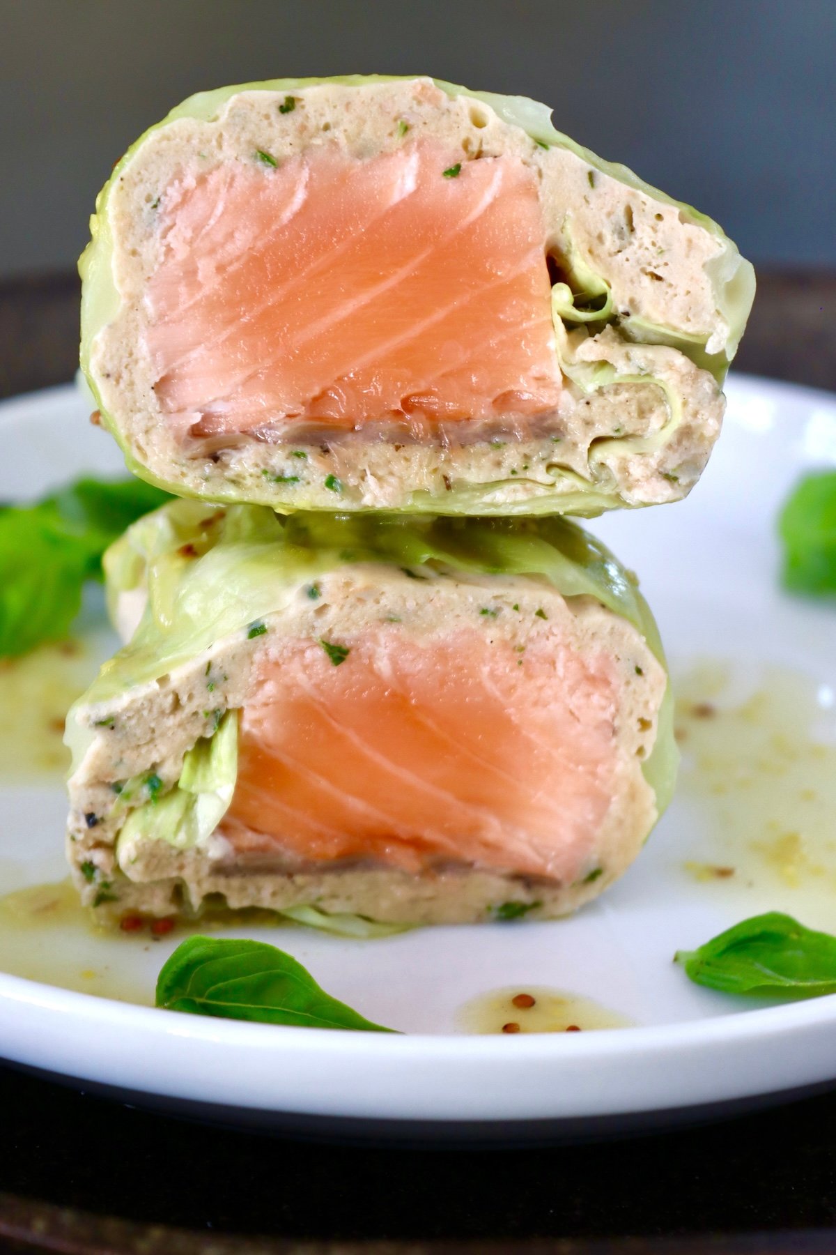Salmon-and-Cabbage-Recipe One salmon cabbage roll cut in half, with cross section shown on a white plate with basil leaves.