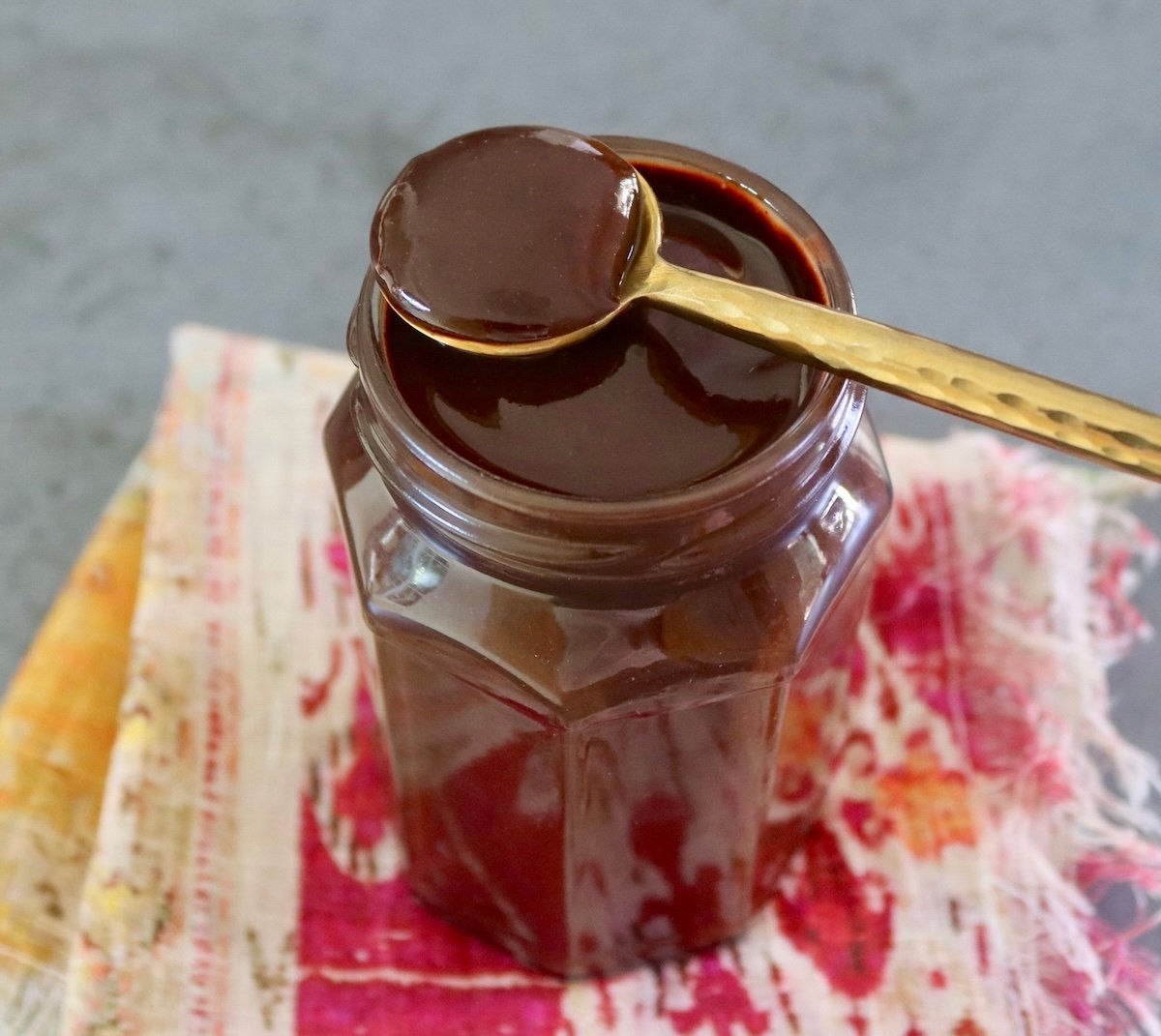 Jar with espresso chocolate sauce, with a gold spoon resting on top.