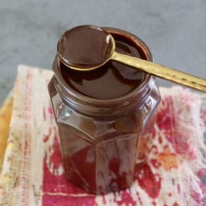 Jar with espresso chocolate sauce, with a gold spoon resting on top.