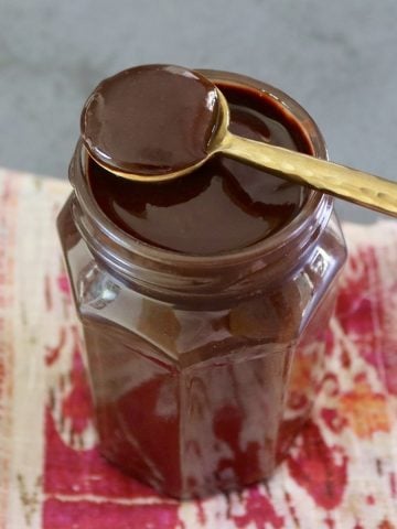 Jar with espresso chocolate sauce, with a gold spoon resting on top.