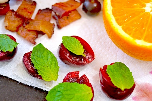 A few halved cherries with mint leaves on top of them on a paper towel.