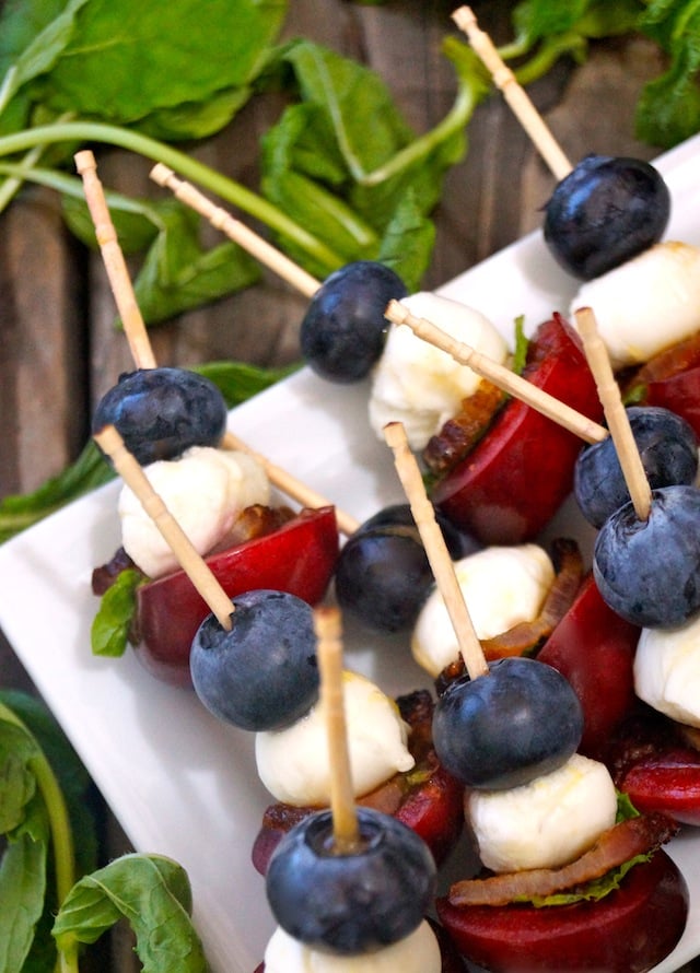 Mini Fruit Skewers on a square white plate with fresh basil.
