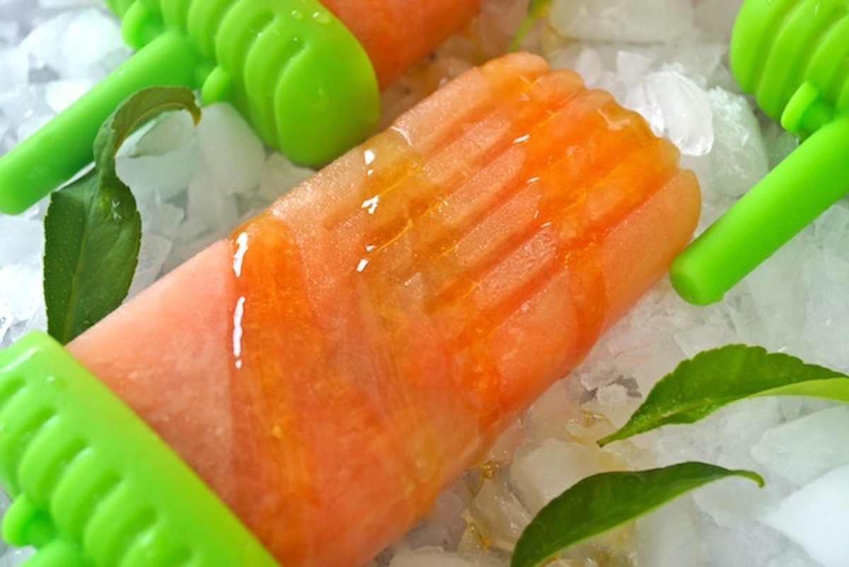 Grapefruit-Popsicle-Recipe-with-Honey One grapefruit popsicle on ice with a drizzle of honey.