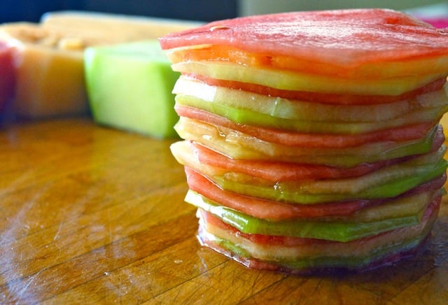 Stack of thinly sliced melon of varying colors on cutting board