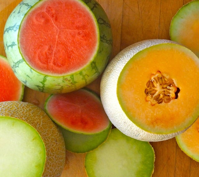 Several melons on cutting board with tops cut off