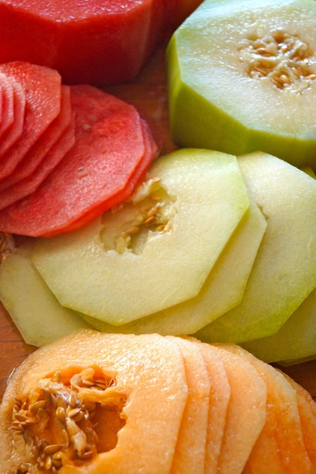 Thin slices of watermelon, orange and green melon on a cutting board