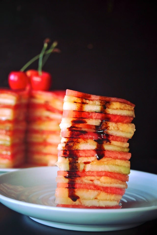 tall slice of Fresh Melon Cake with balsamic glaze on a white plate with cake behind it