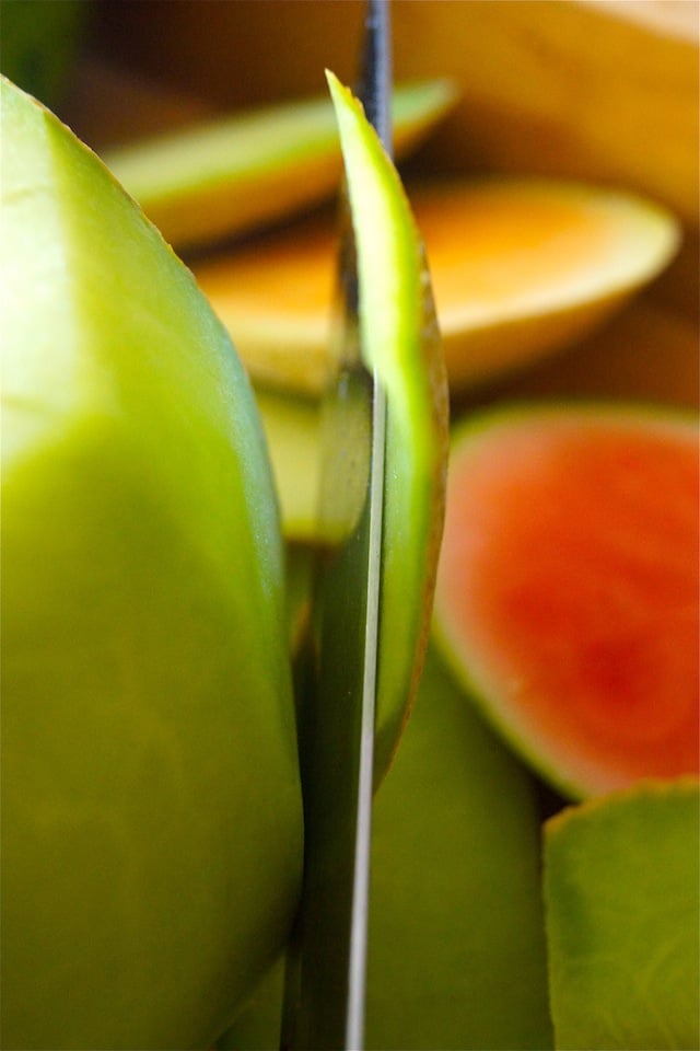 Green melon with a Chef's knife slicing off the skin