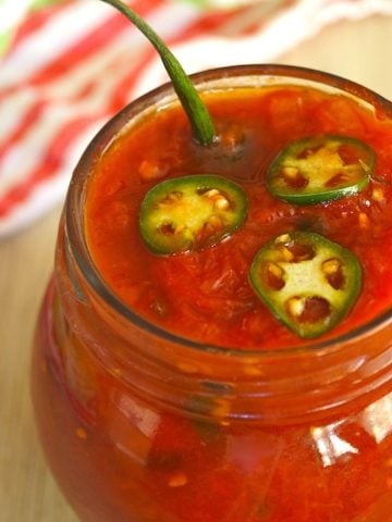 Spicy Serrano-Tomato Preservesin a round jar with serrano stem poking out.