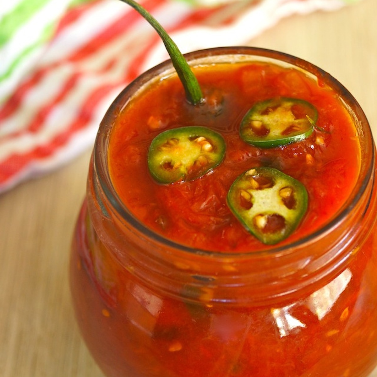 Spicy Serrano-Tomato Preservesin a round jar with serrano stem poking out.