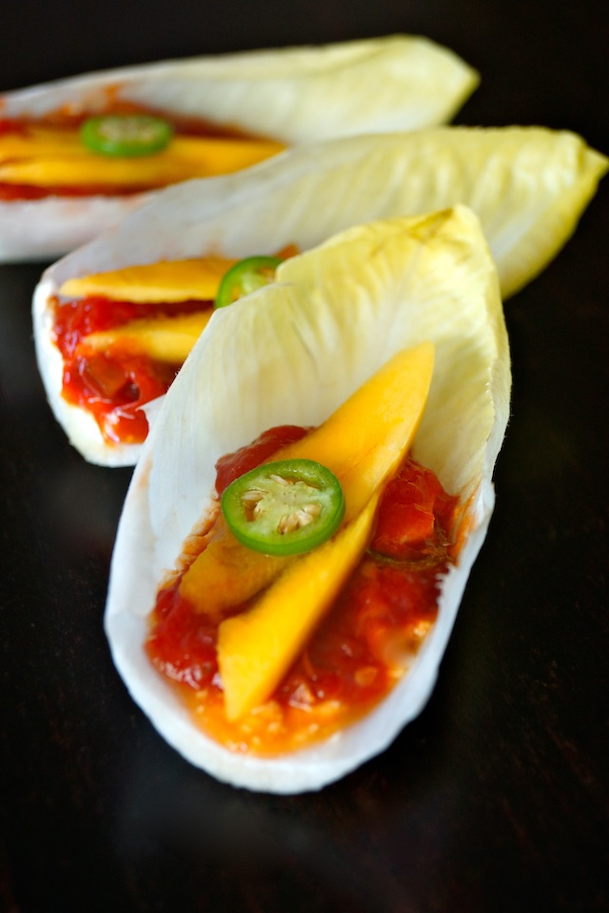 A few endive leaves holding tomato preserves and mango slices.