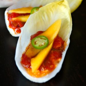A few endive leaves holding tomato preserves and mango slices.