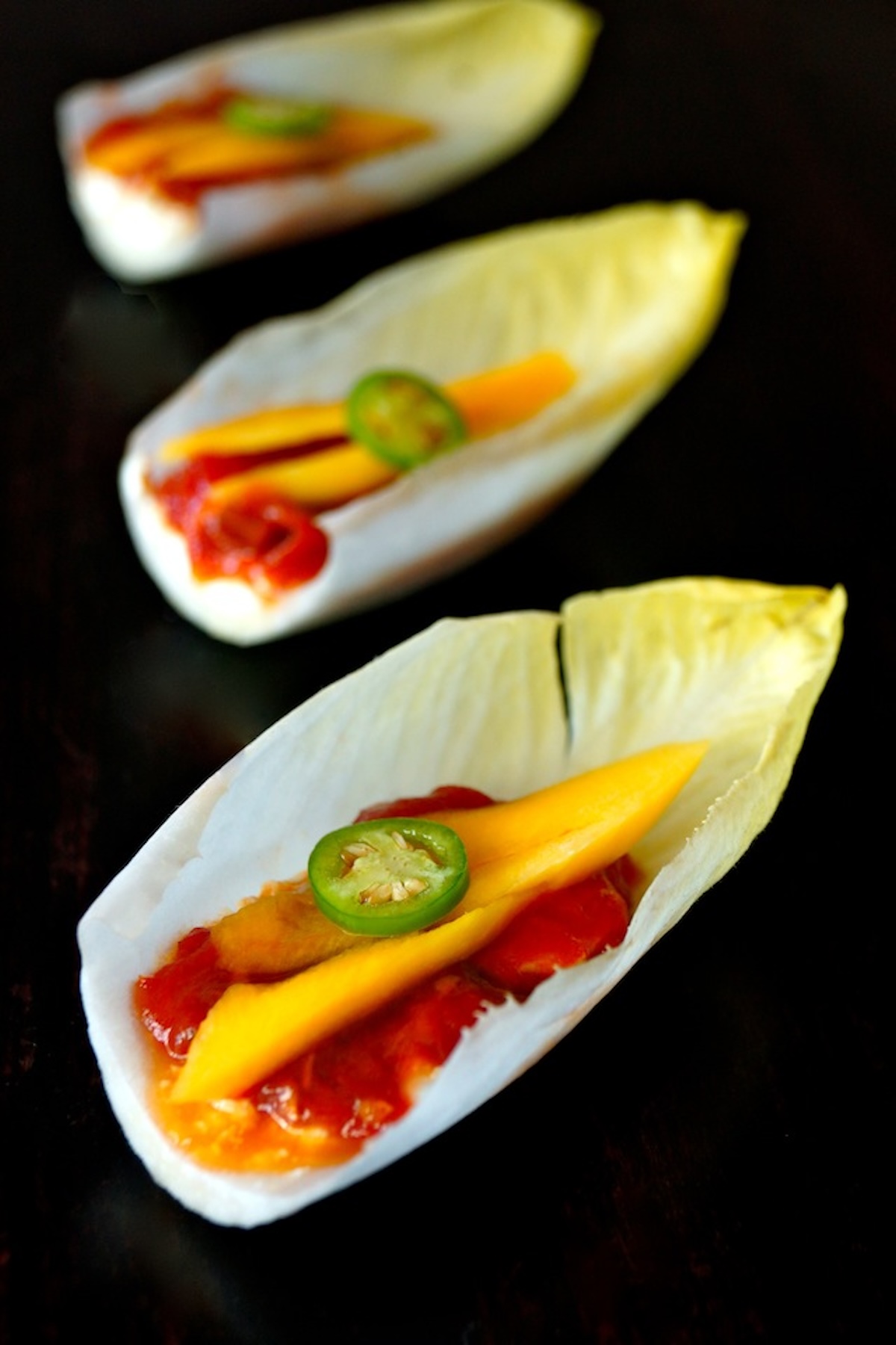 A few endive leaves holding tomato preserves and mango slices.