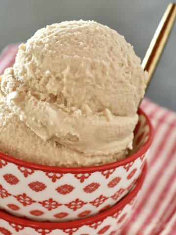 Two little stacked red and white bowls with a couple of scoops of root beer float ice cream and a gold spoon.