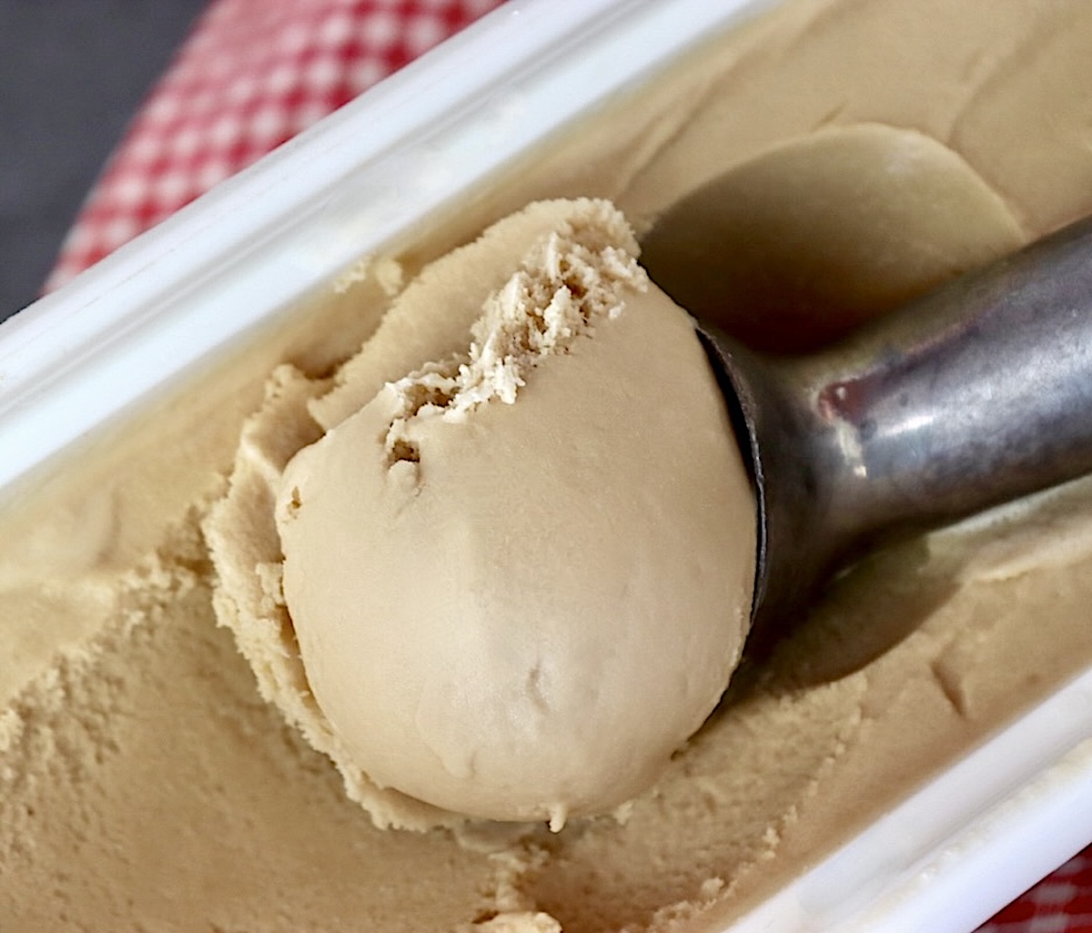 Root beer ice cream being scooped from white container.