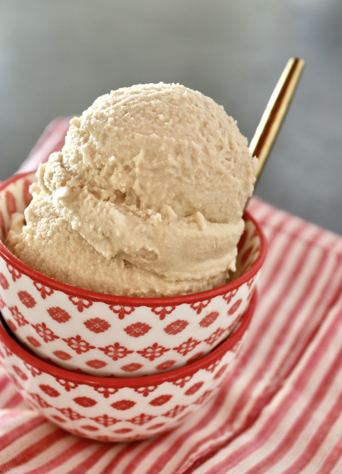 Two little stacked red and white bowls with a couple of scoops of root beer float ice cream and a gold spoon.