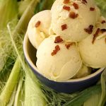 Four scoops of corn ice cream in a purple bowl, surrounded by corn husks.