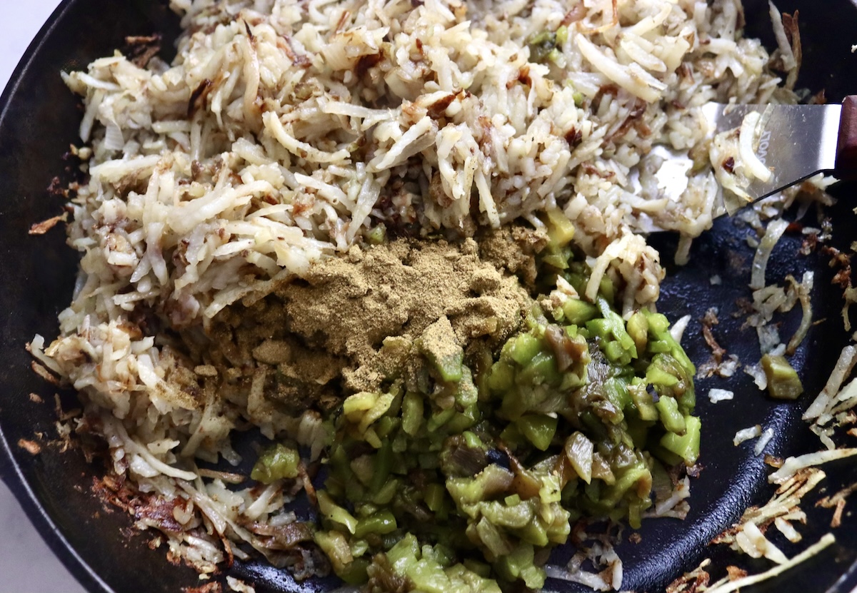 Browned grated potatoes in a cast iron skillet with roasted and chopped Hatch chiles and spices.