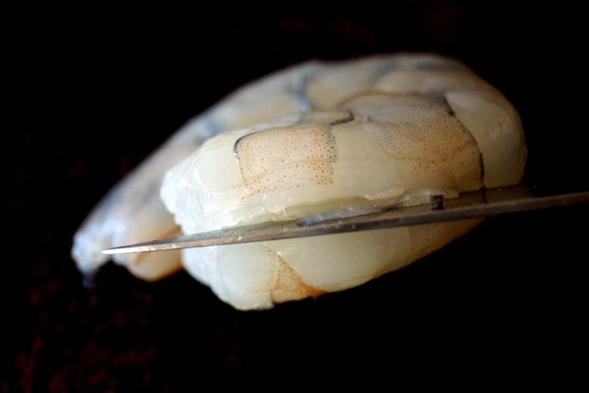 Paring knife slicing into a raw shrimp, along the side.