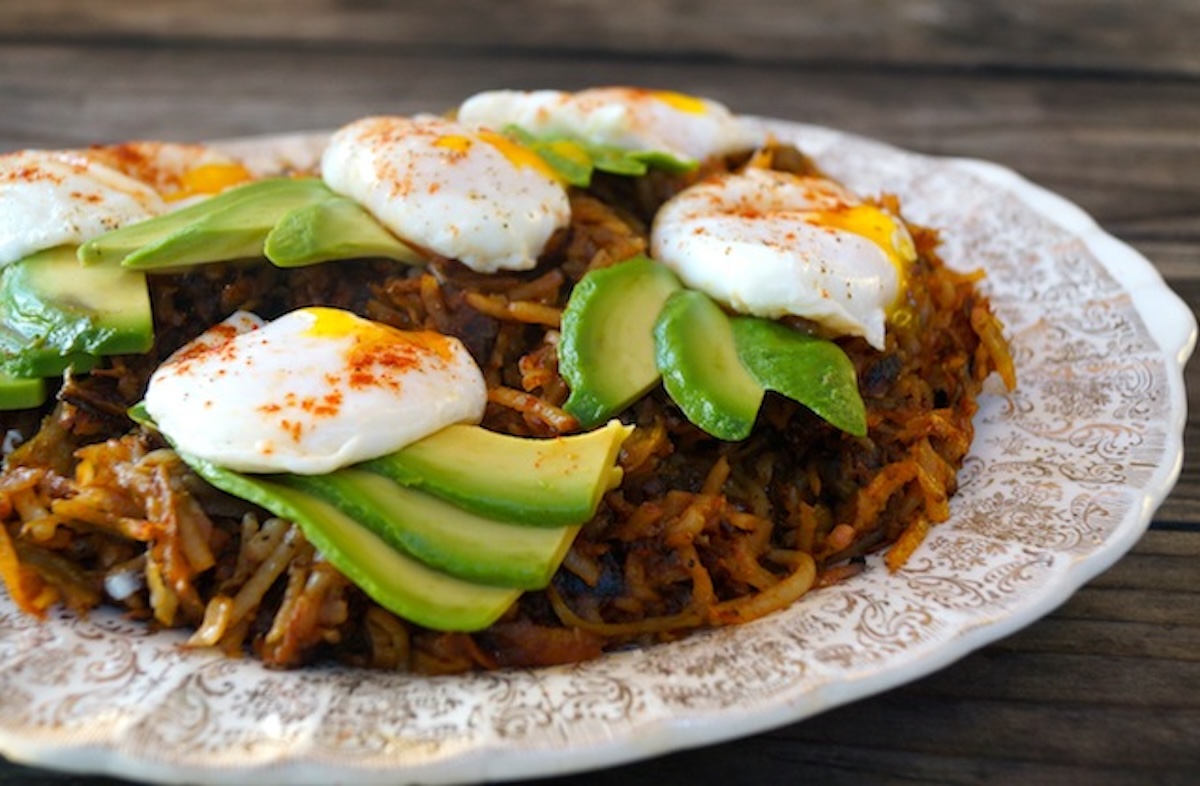 Hash browns on a cream-colored plate with perfect poached eggs and avocado slices on top.