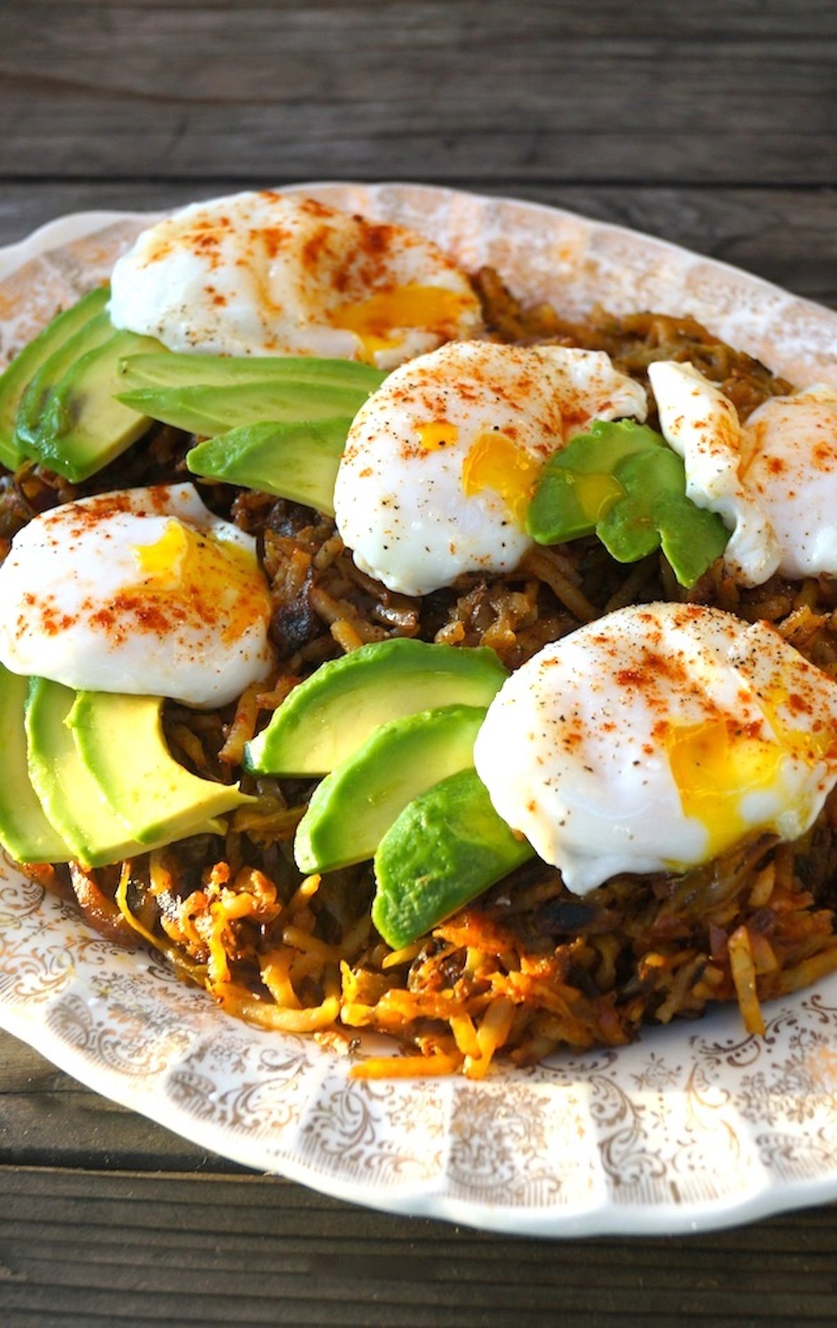 Hash browns on a cream-colored plate with perfect poached eggs and avocado slices on top.