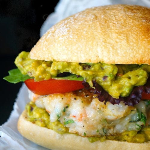 close up of shrimp burger with guacamole in a bun on parchment paper