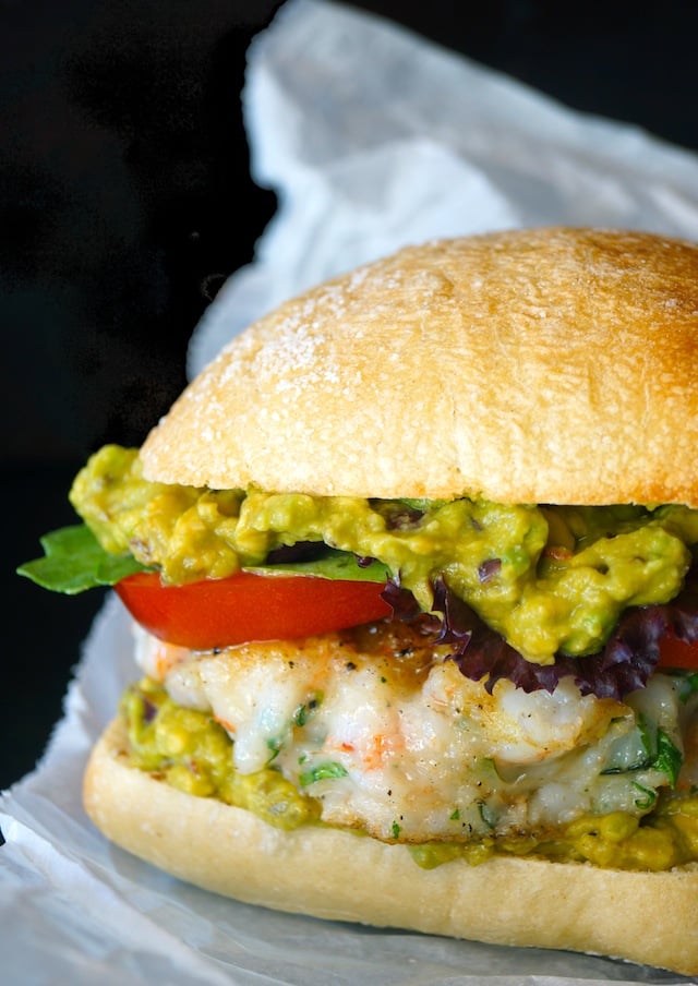 Shrimp burger with guacamole, tomato, lettuce and bun on parchment paper.