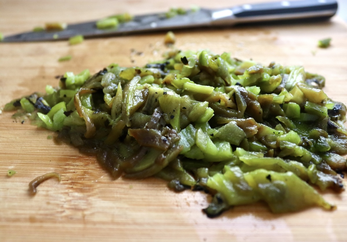 Pile of roughly chopped roasted hatch chiles and a Chef's knife on a wood cutting board.