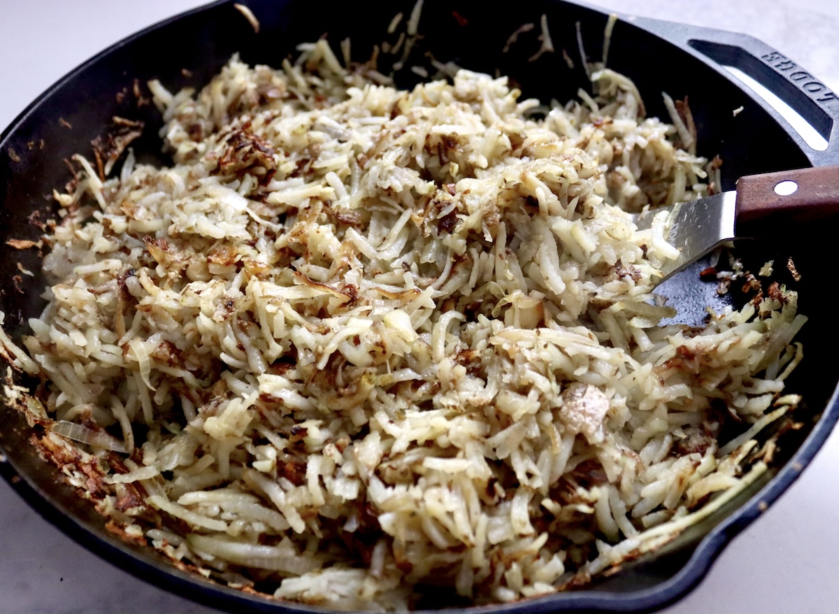 Browned Hatch Browns in a cast iron skillet with onion.