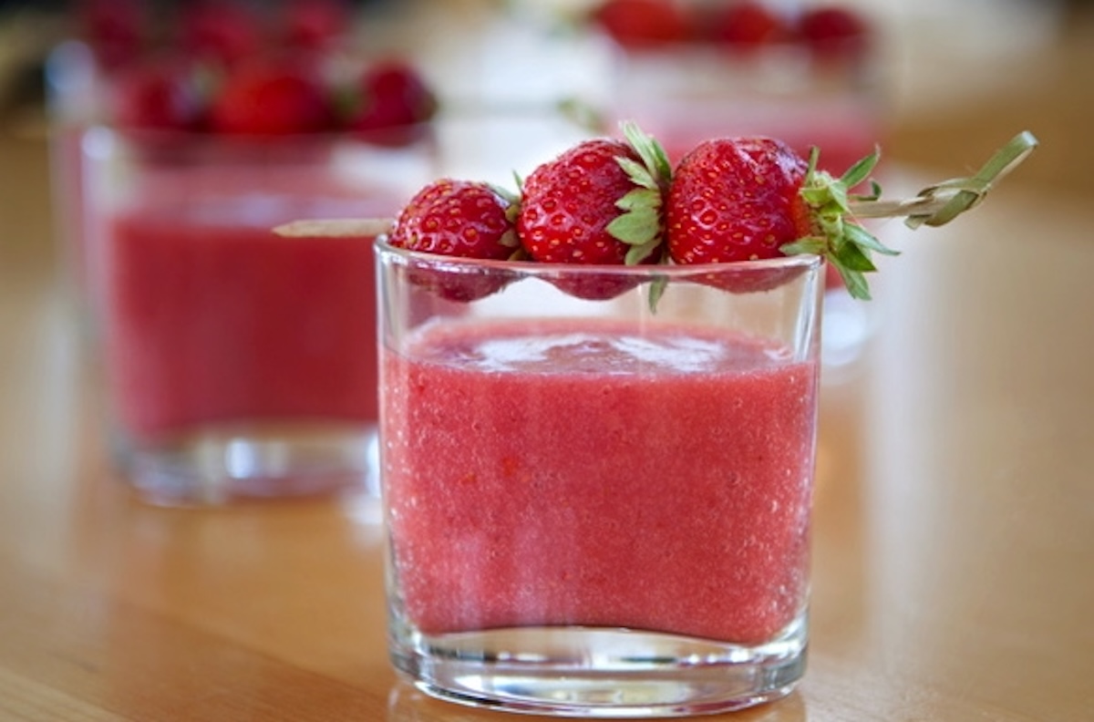Small glass filled with strawberry and tomato gazpacho with tiny strwaberries for garnish.