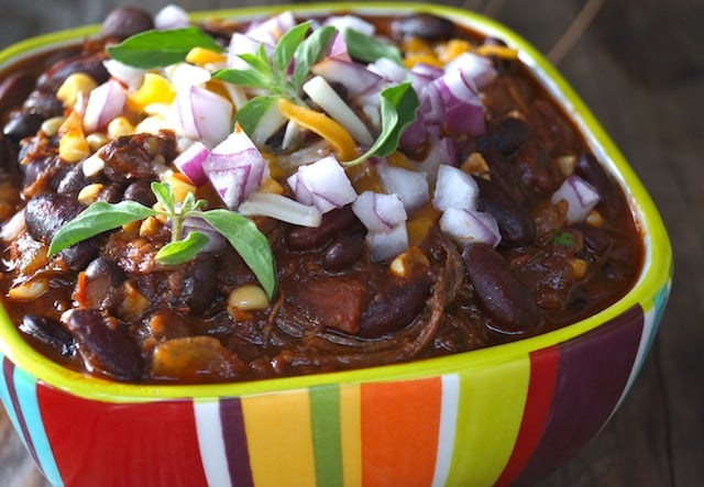 Brisket Chili Recipe in a brightly colored striped bowl, topped with fresh herbs and chopped red onion.