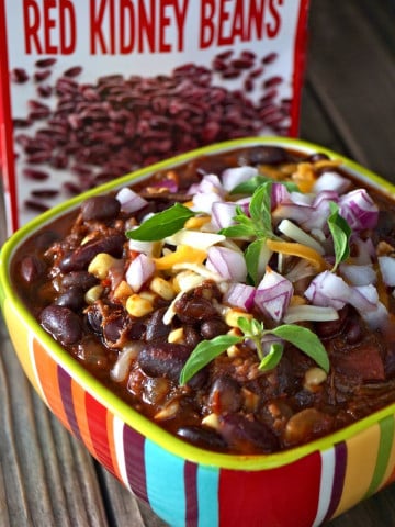 Colorful striped bowl of brisket chili with fresh green herbs and chopped red onion on top.
