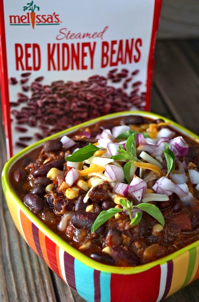 Chipotle Bacon Brisket Chili in a bright-colored striped bowl, with a box of red kidney beans in the background.